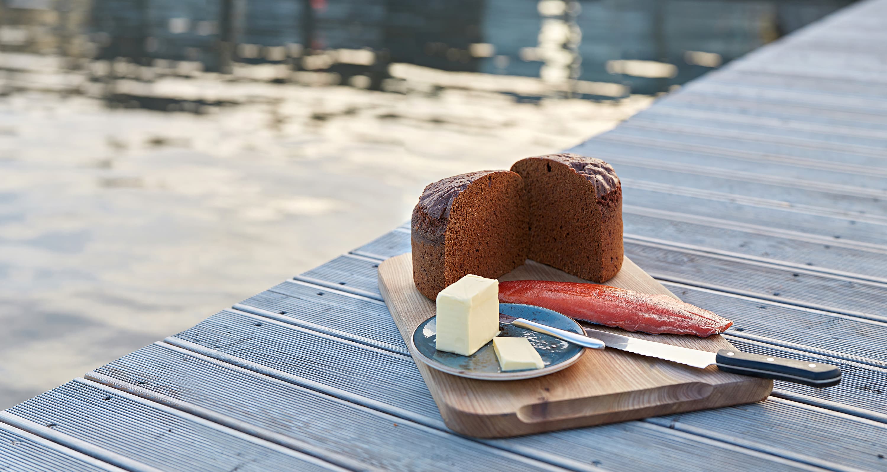 Warm geothermal rye bread with butter on a wooden deck beside the water