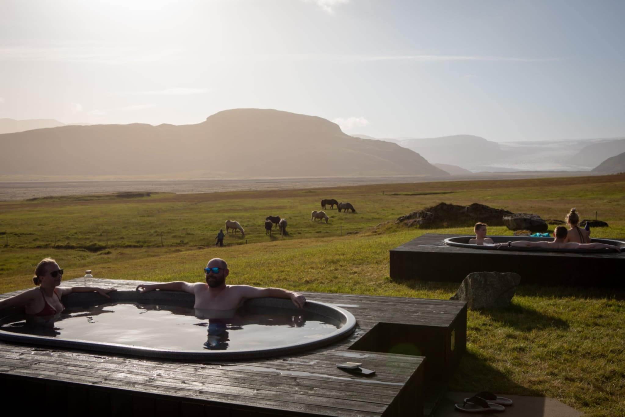 Bathers in a wooden-rimmed hot tub at Hoffell, with a green valley and mountains behind