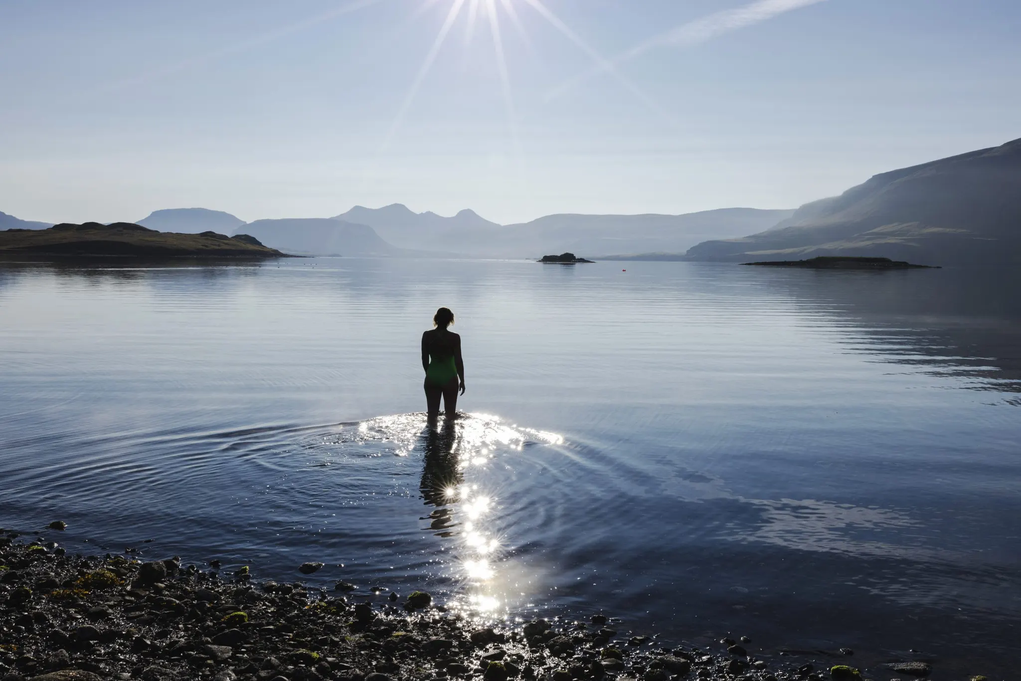 A bather standing in the shallows, mirrored in the fjord