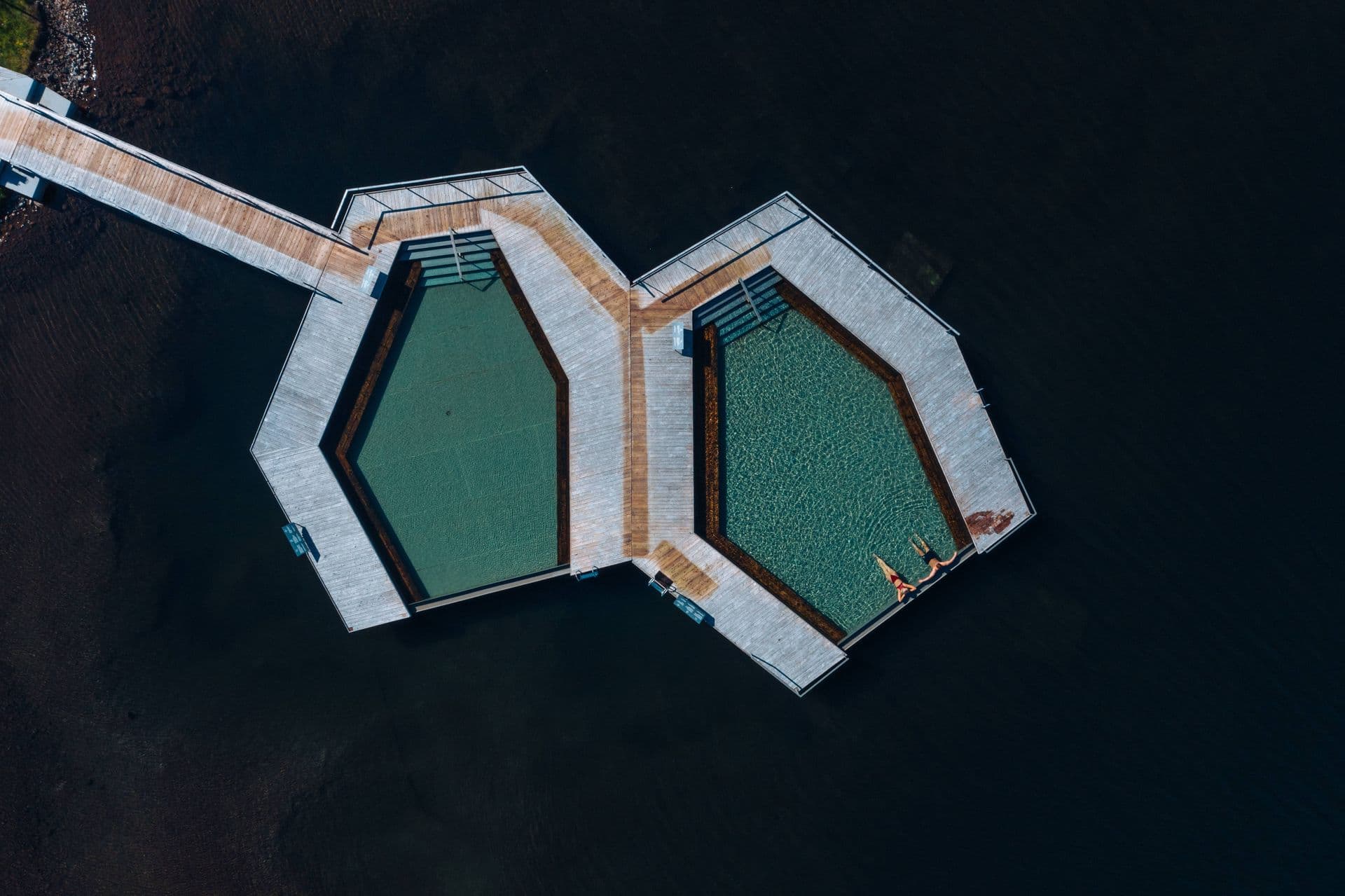 Aerial view of Vök’s two hexagonal floating pools on the dark water of Urriðavatn