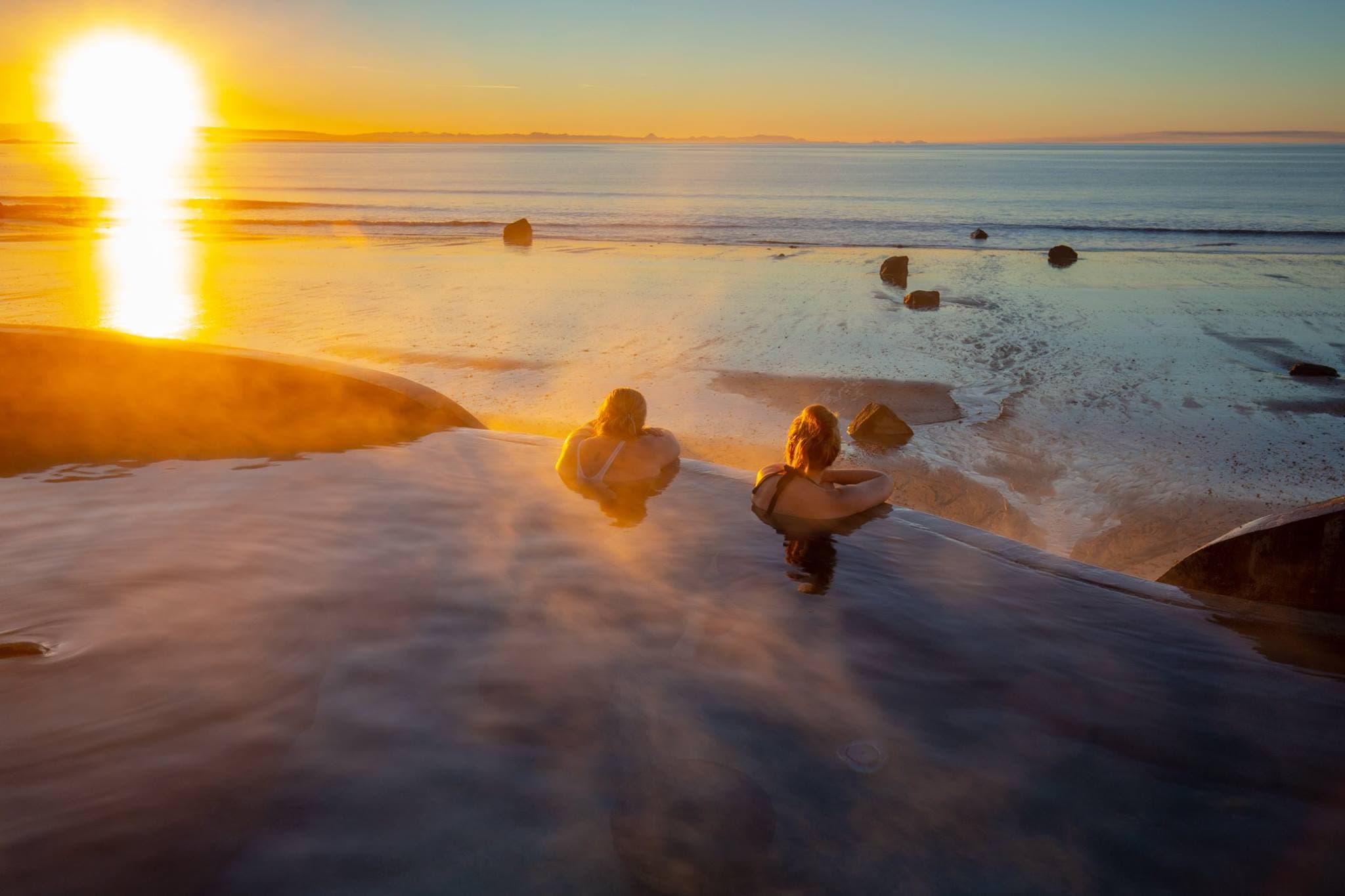Bathers in Guðlaug’s hot pool in low sun, with the sea beyond