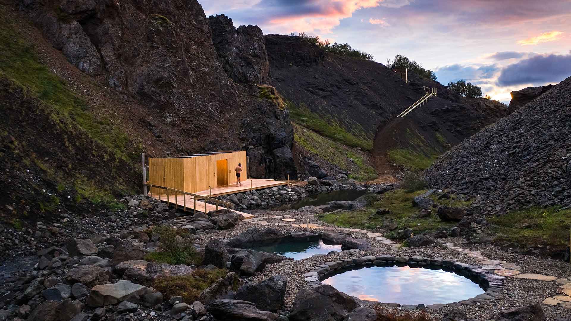 A timber bathhouse beside a round stone pool in Hringsgil canyon at dusk