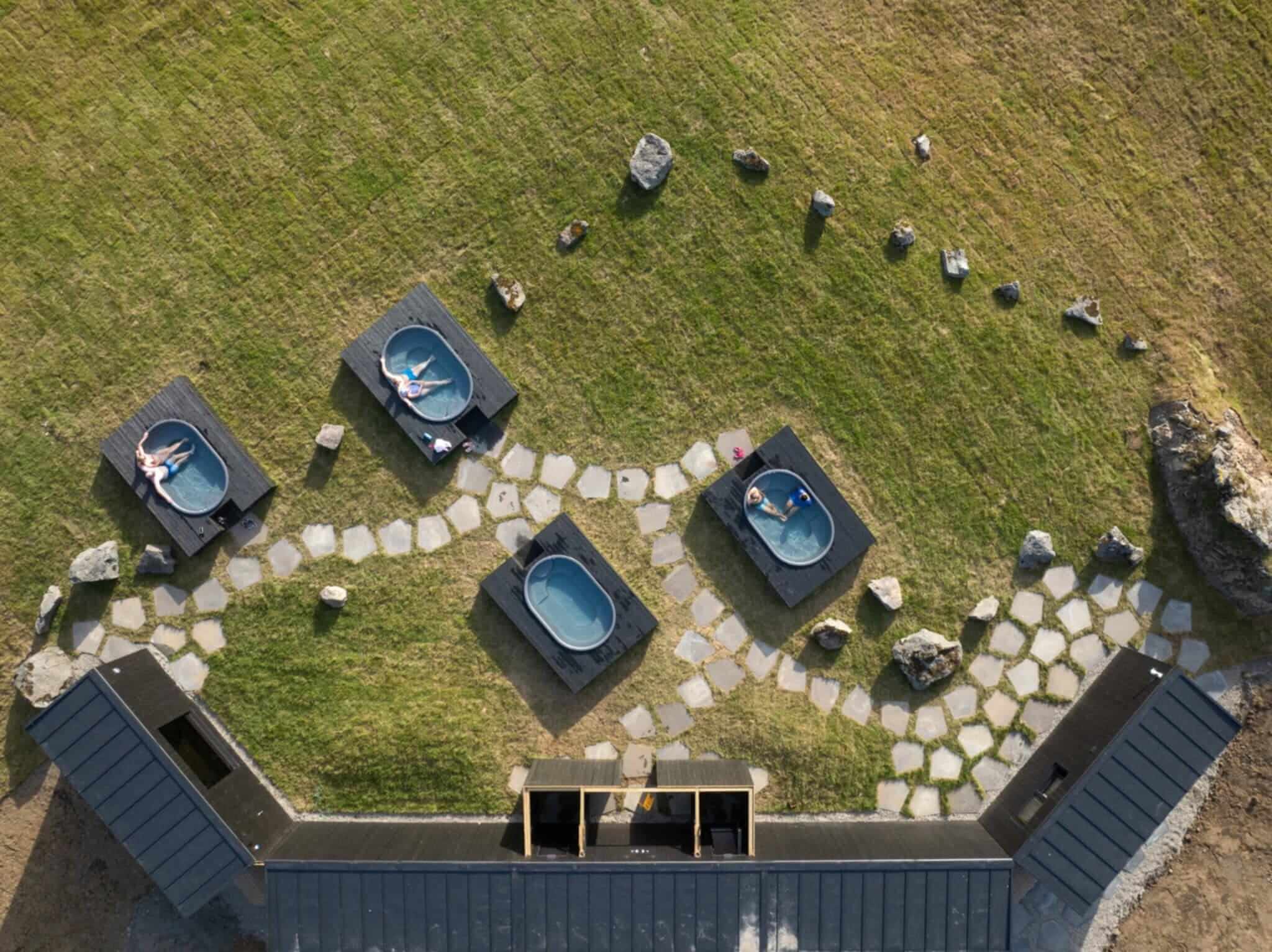 Aerial view of four dark hot tubs linked by a stone path in the grass