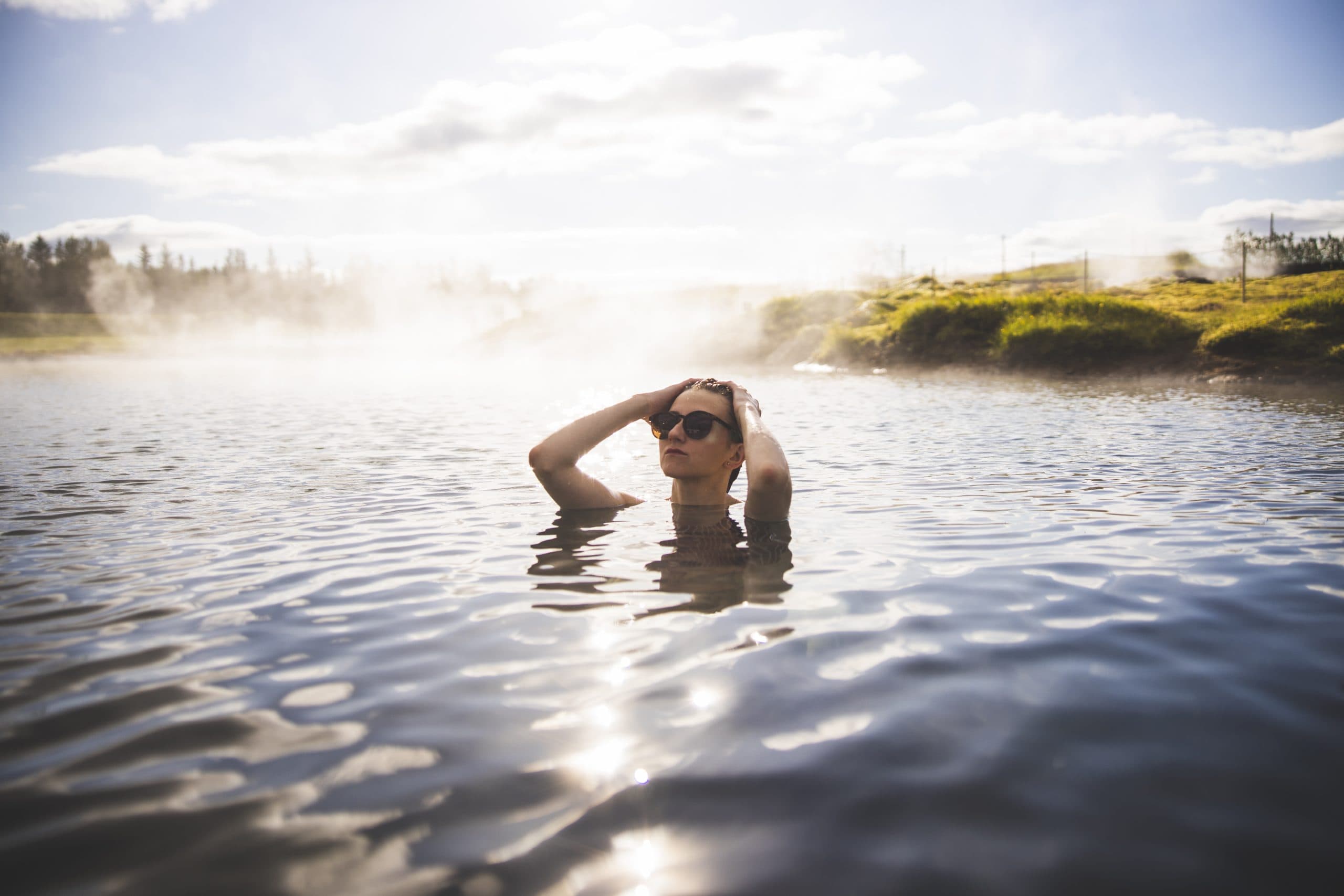 A woman bathing in the steaming lagoon with a hazy landscape behind