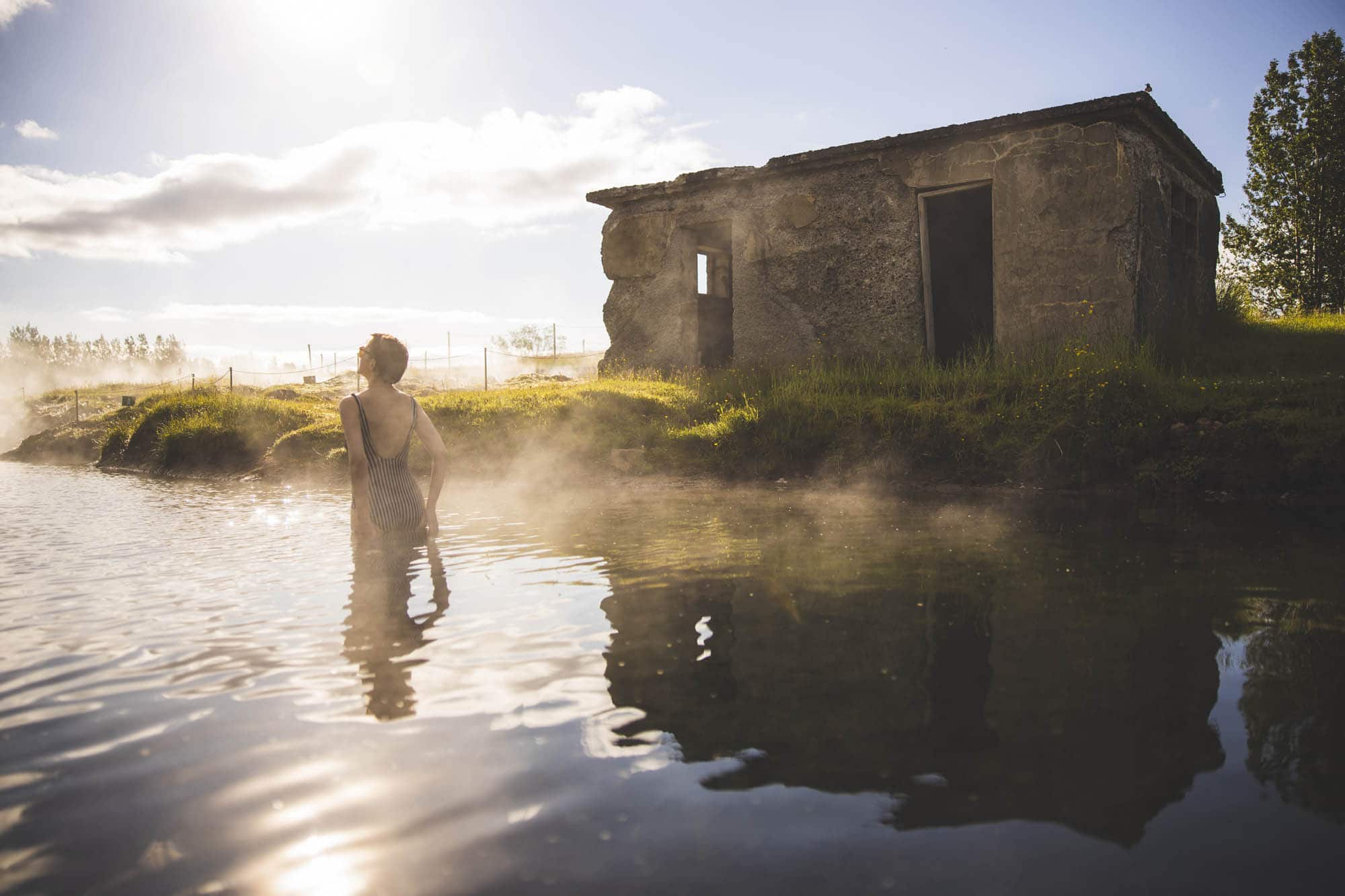 A bather in the shallow, steaming pool in front of the old stone building