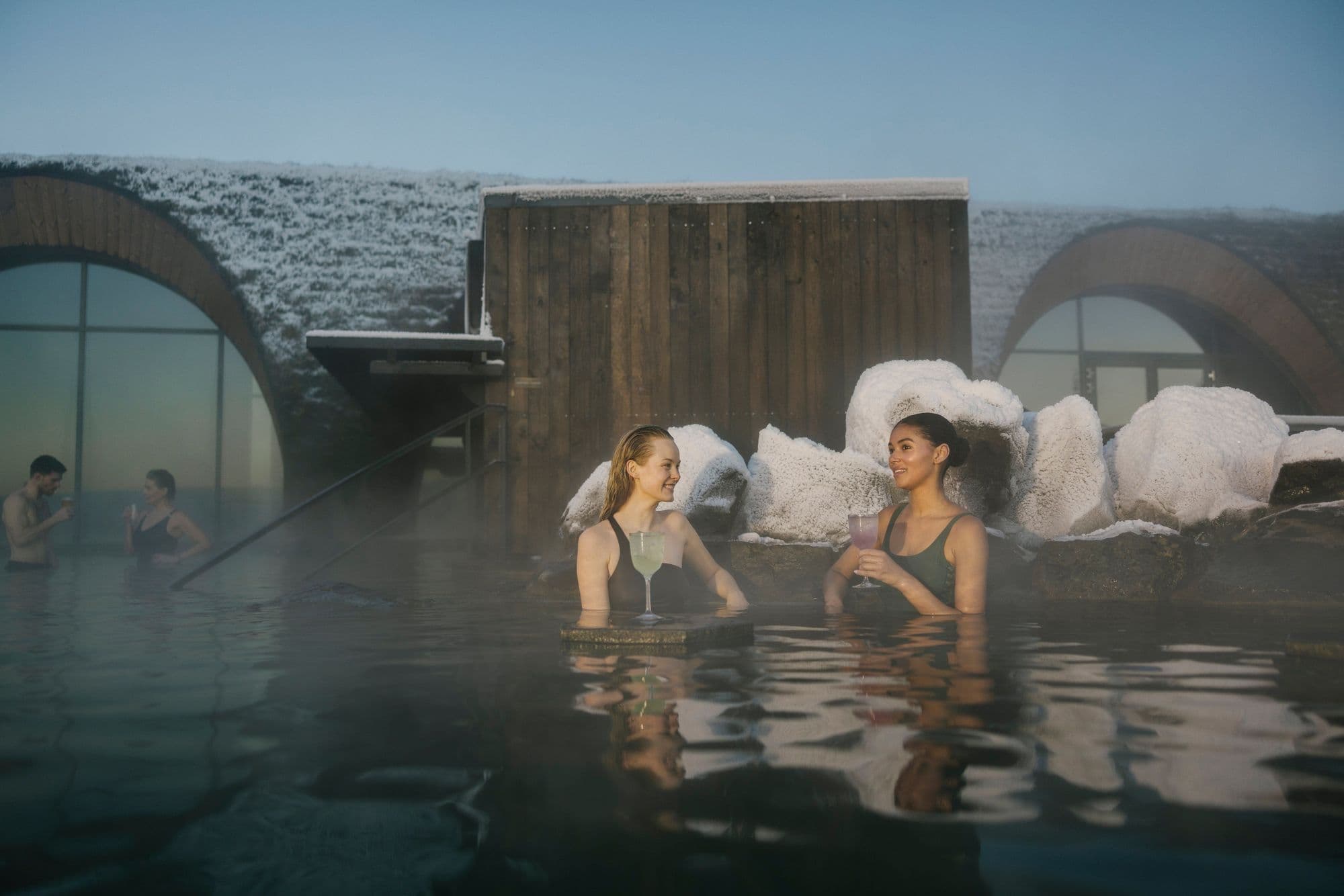 Two bathers by the lagoon’s stone-arched walls and bar, with snow on the roofs