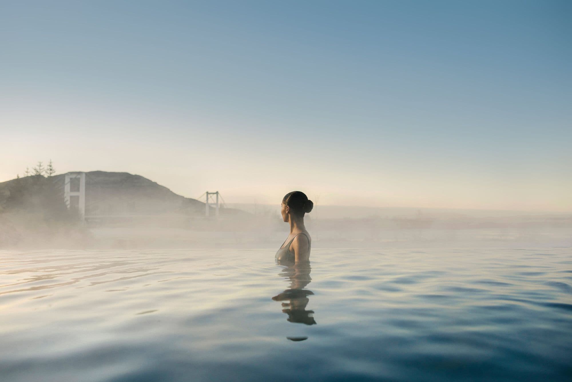 A bather at the infinity edge, looking over misty water to the mountains