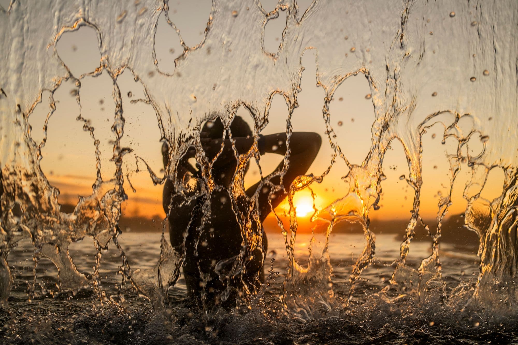 A bather silhouetted behind the waterfall at Laugarás Lagoon at sunset